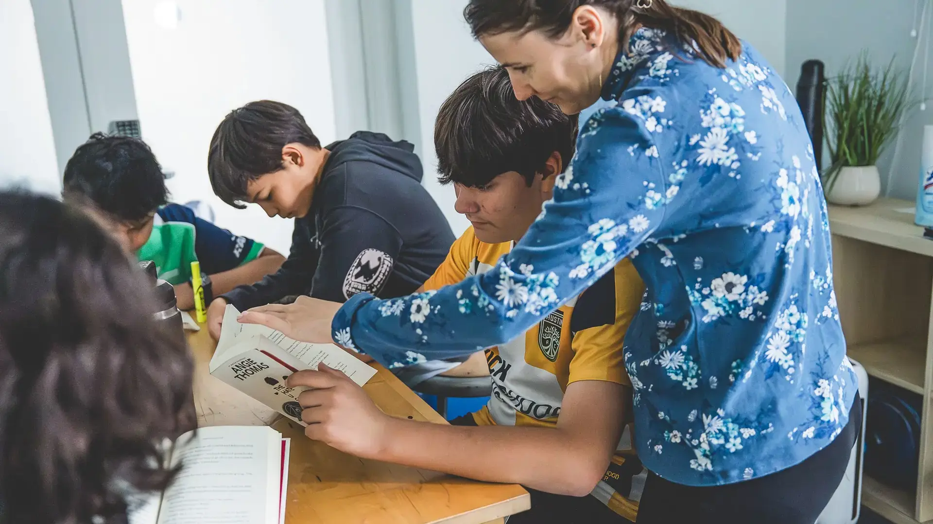 a teacher pointing to a book while guiding middle school students during a reading lesson.