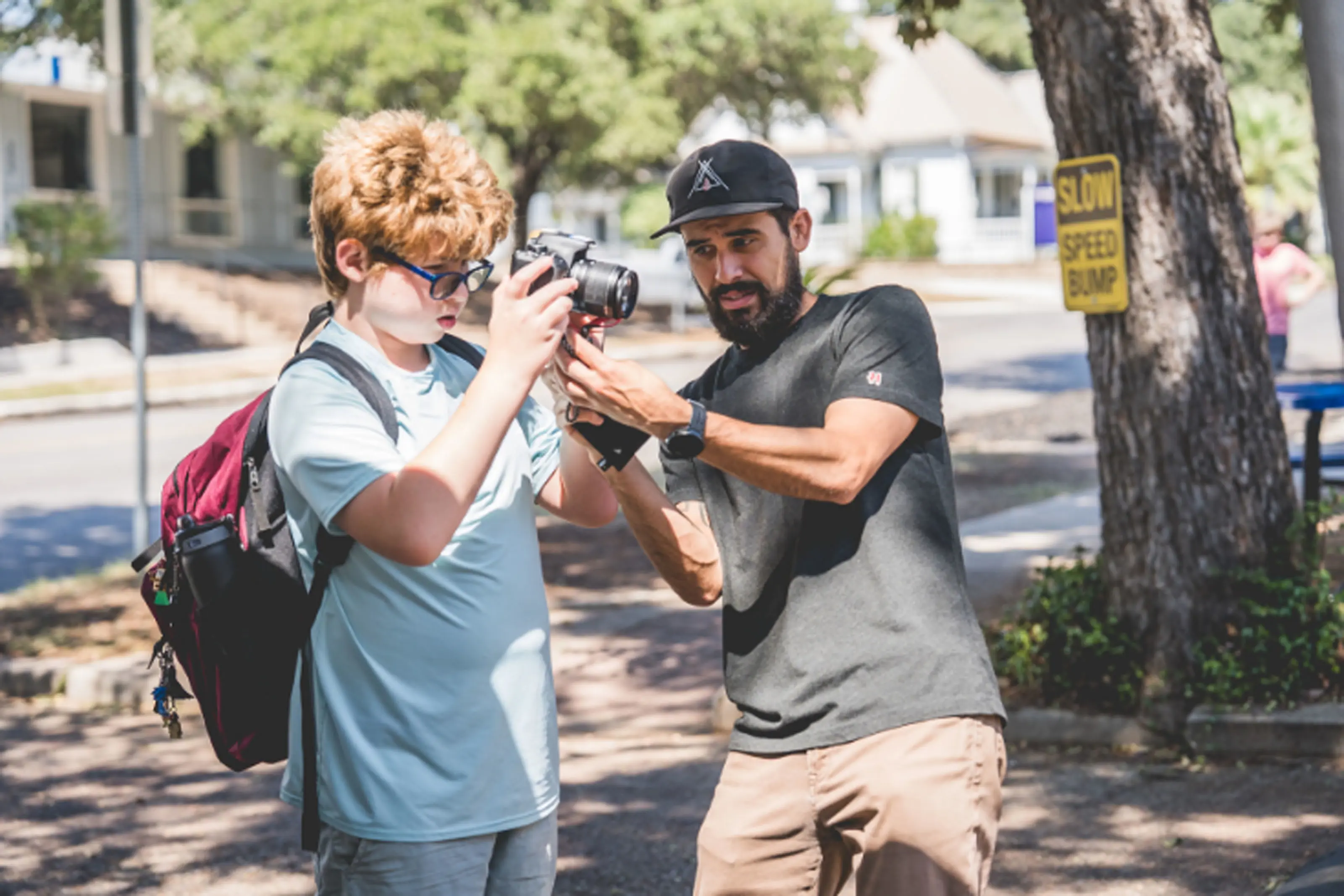 teacher helping a middle school student hold a DSLR camera outdoors during a photography lesson.
