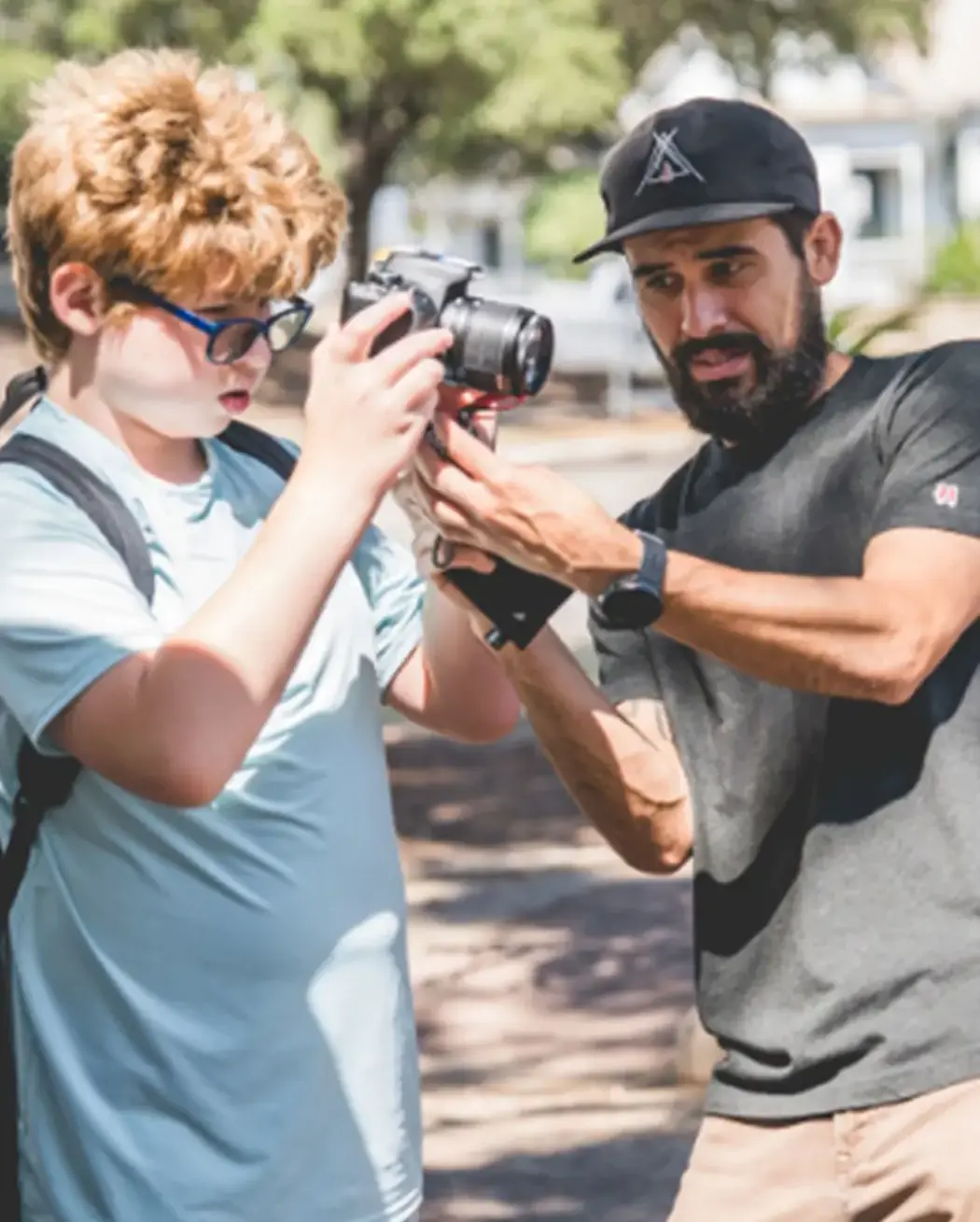 A teacher guiding a middle school student using a camera outdoors.