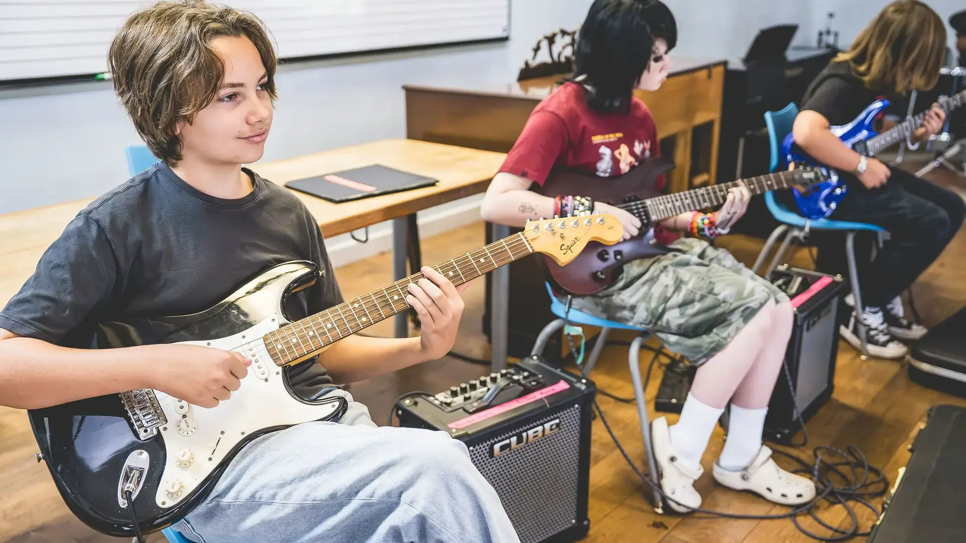 middle school students playing guitar and bass together in music class.