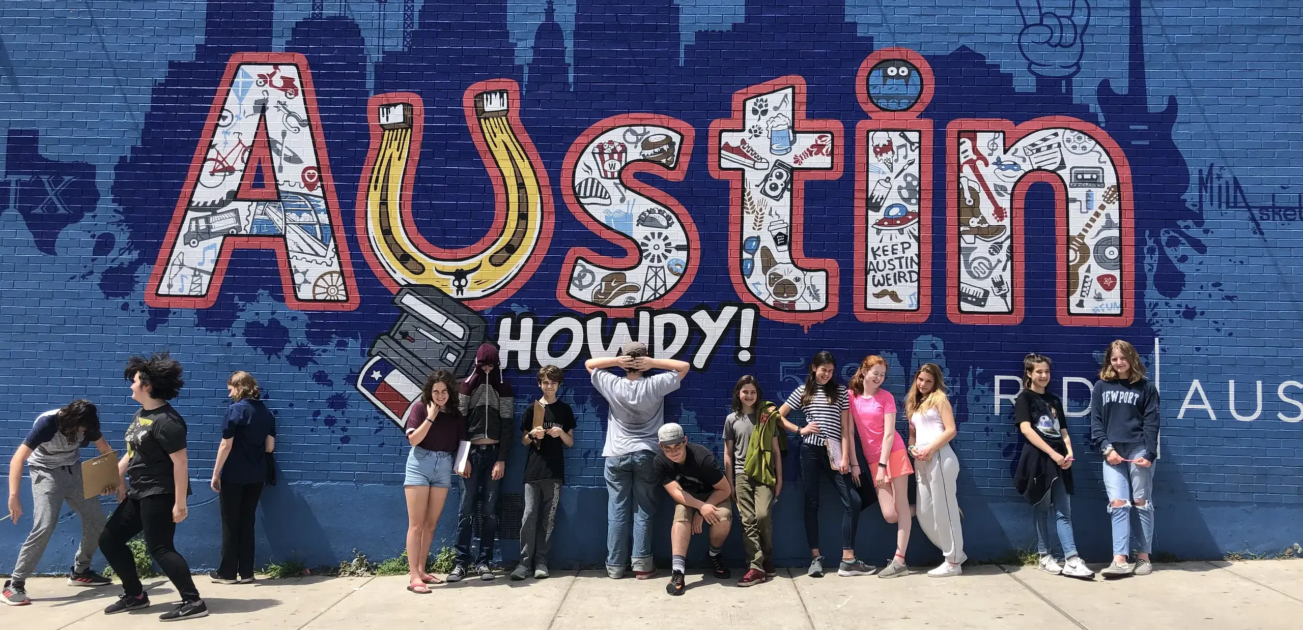 Middle school students posing in front of a colorful 'Austin Howdy' mural during a city-as-classroom field study.