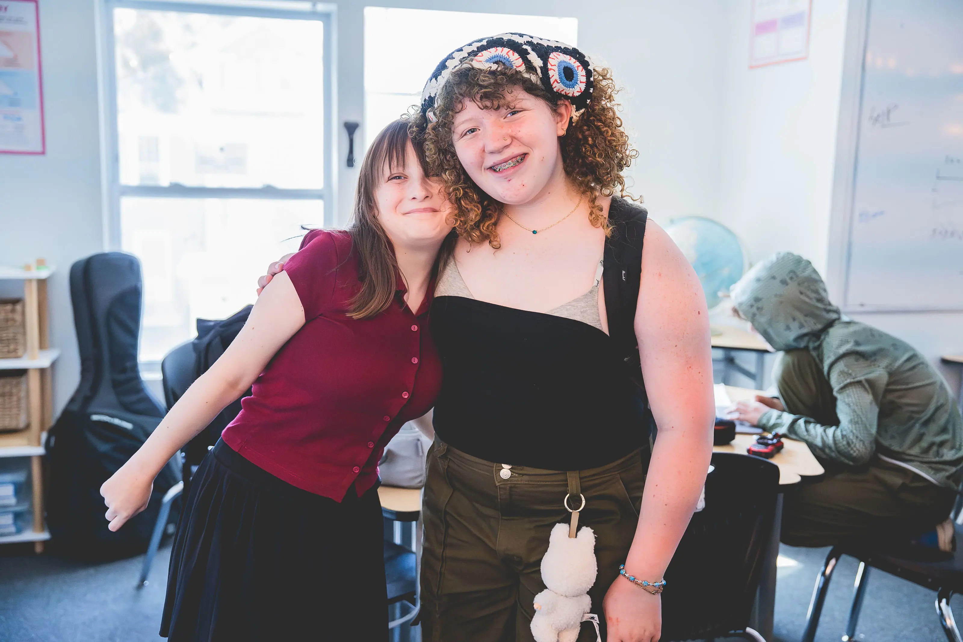 two middle school students smiling with an arm around each other in the classroom.