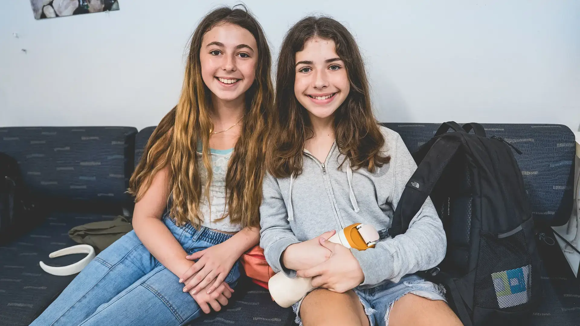 Two middle school students smiling and sitting together indoors.