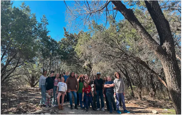 Middle school students and teacher exploring wooded trail during outdoor education.