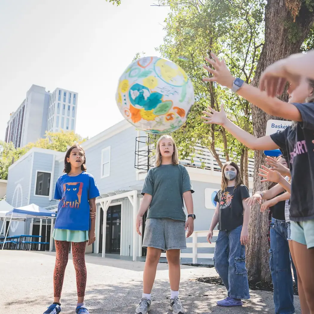 Group of middle school students tossing a ball together outside on campus.