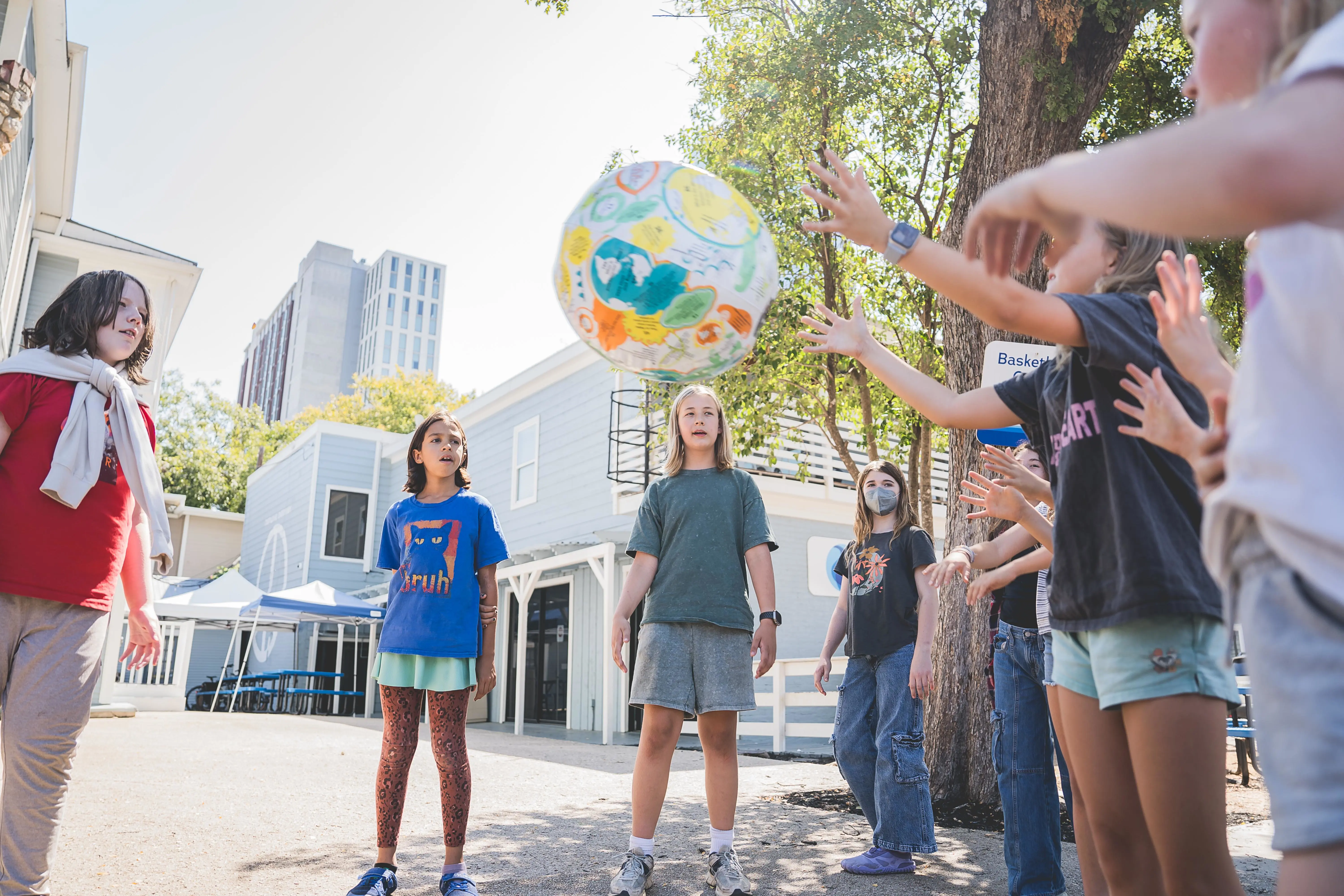 students playing with a large decorated ball outdoors near school buildings.