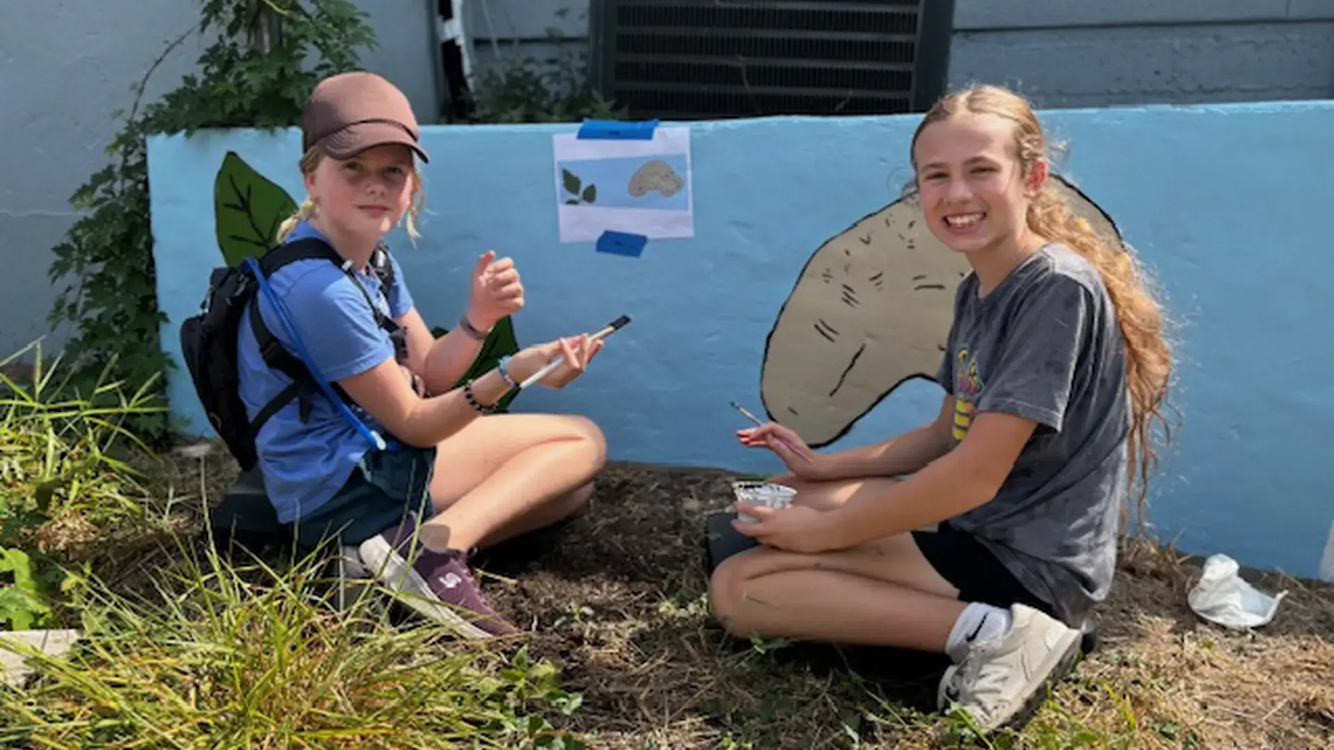 middle school students painting a mural on a campus wall.