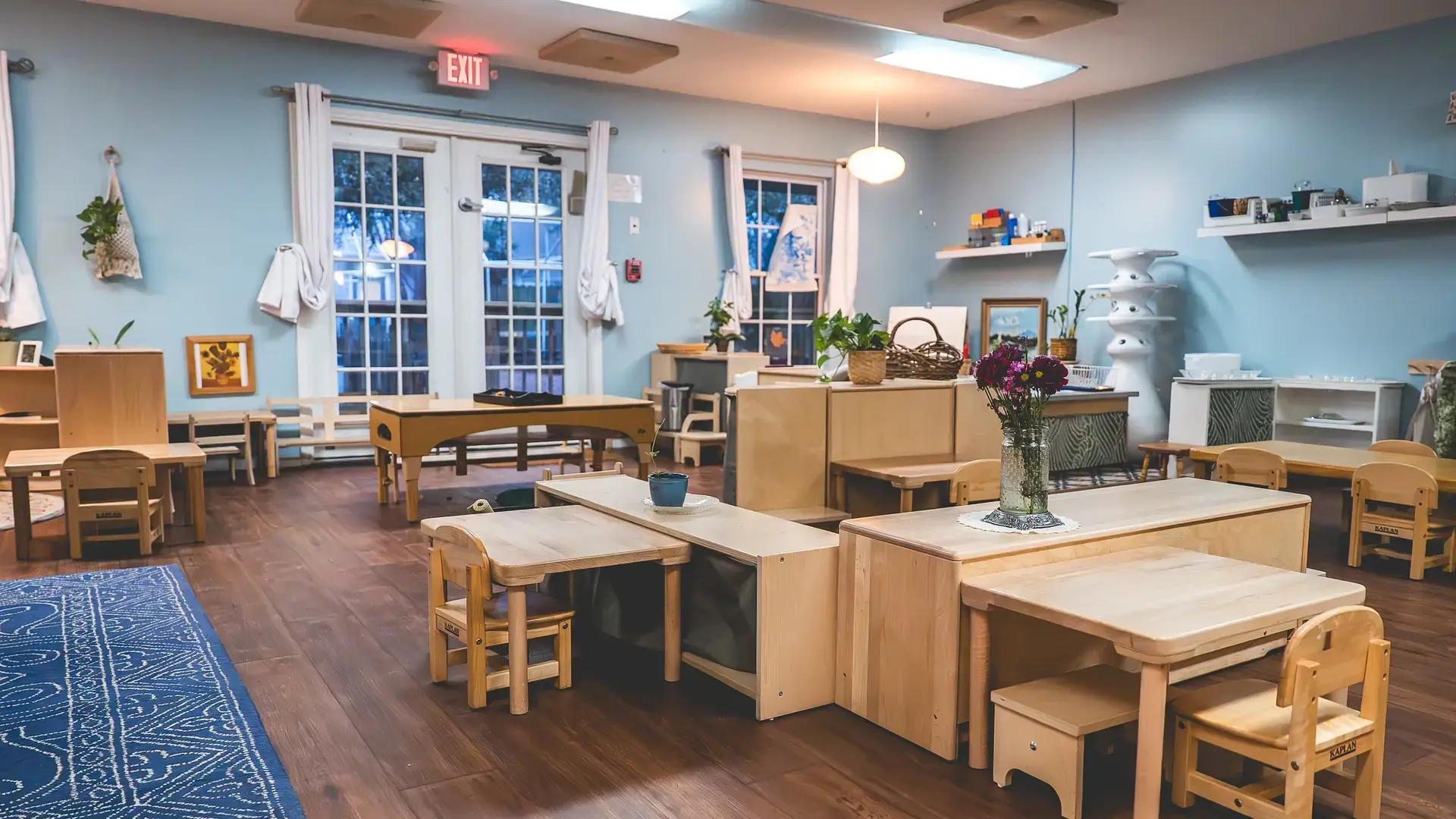 Empty Montessori classroom with low tables and shelves arranged for early childhood learning.