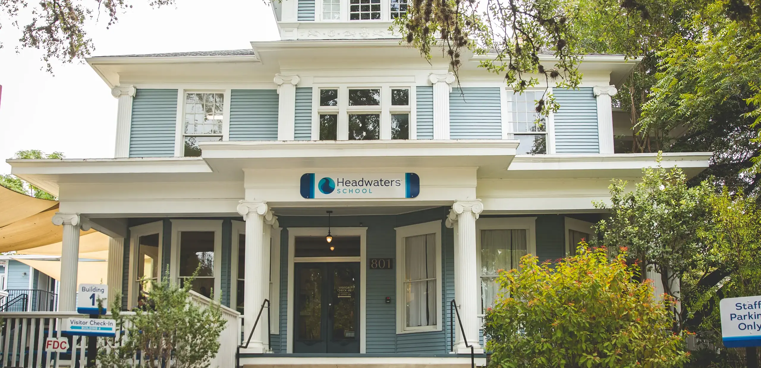 Front entrance of Headwaters School's historic blue Victorian building, Building 1, with visitor check-in signage.