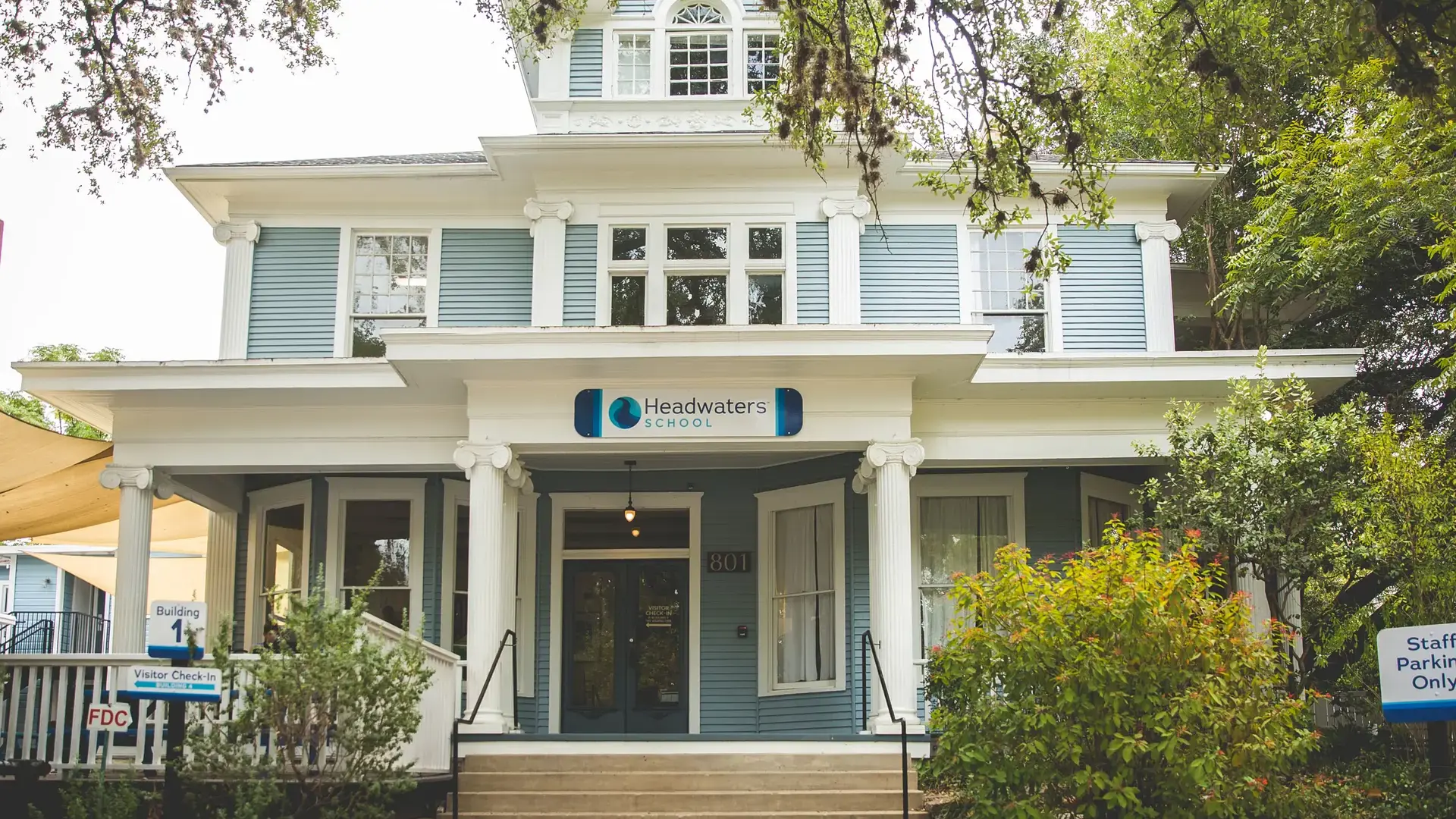 Front entrance of Headwaters School's blue Victorian building surrounded by trees.