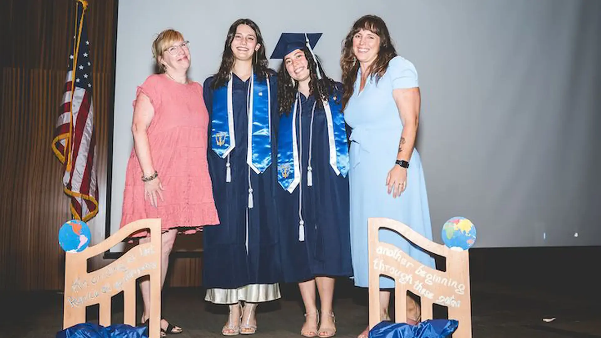 Graduates in caps and gowns posing with family members on stage.