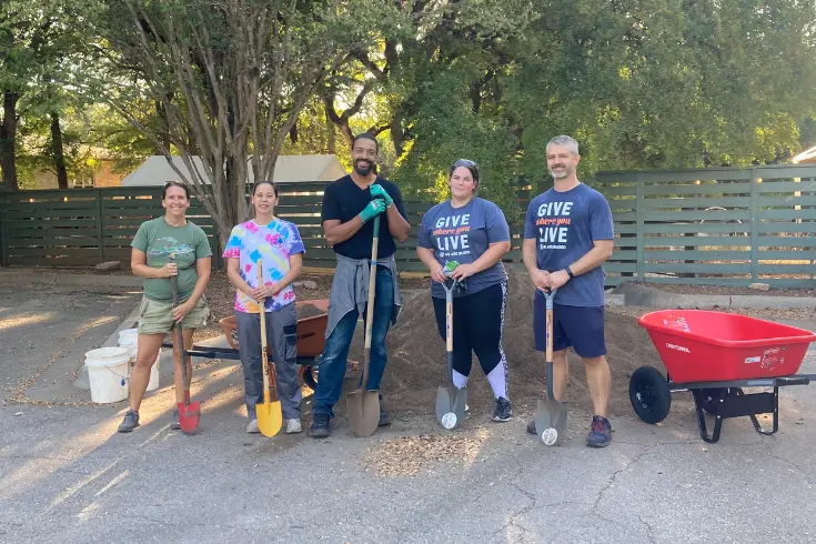 parent volunteers holding shovels and posing together during a school landscaping project.