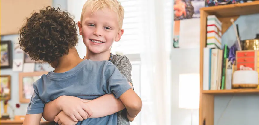 young elementary student smiling while hugging a classmate in the classroom.