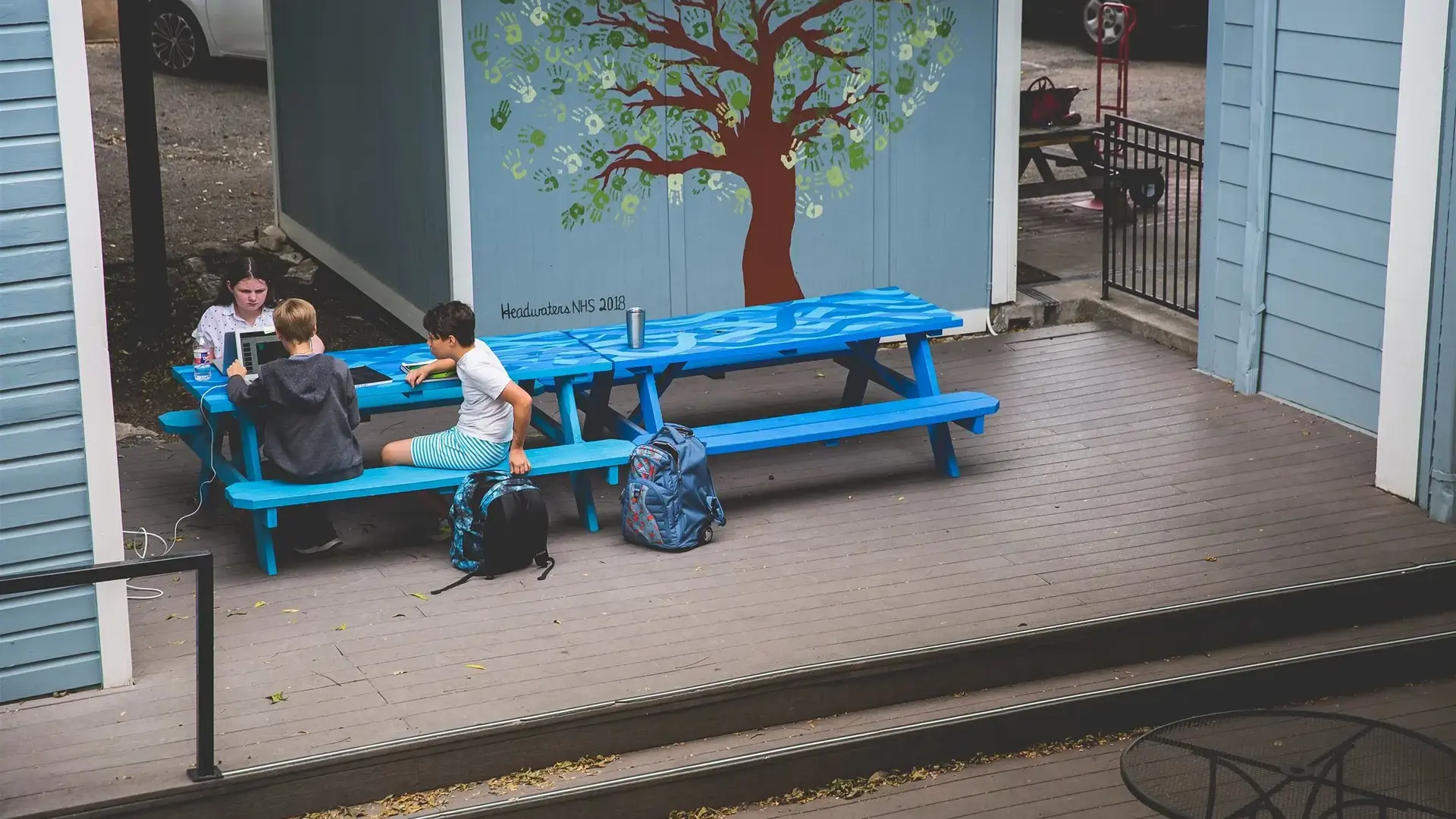 Students sitting at a blue picnic table on an outdoor porch.