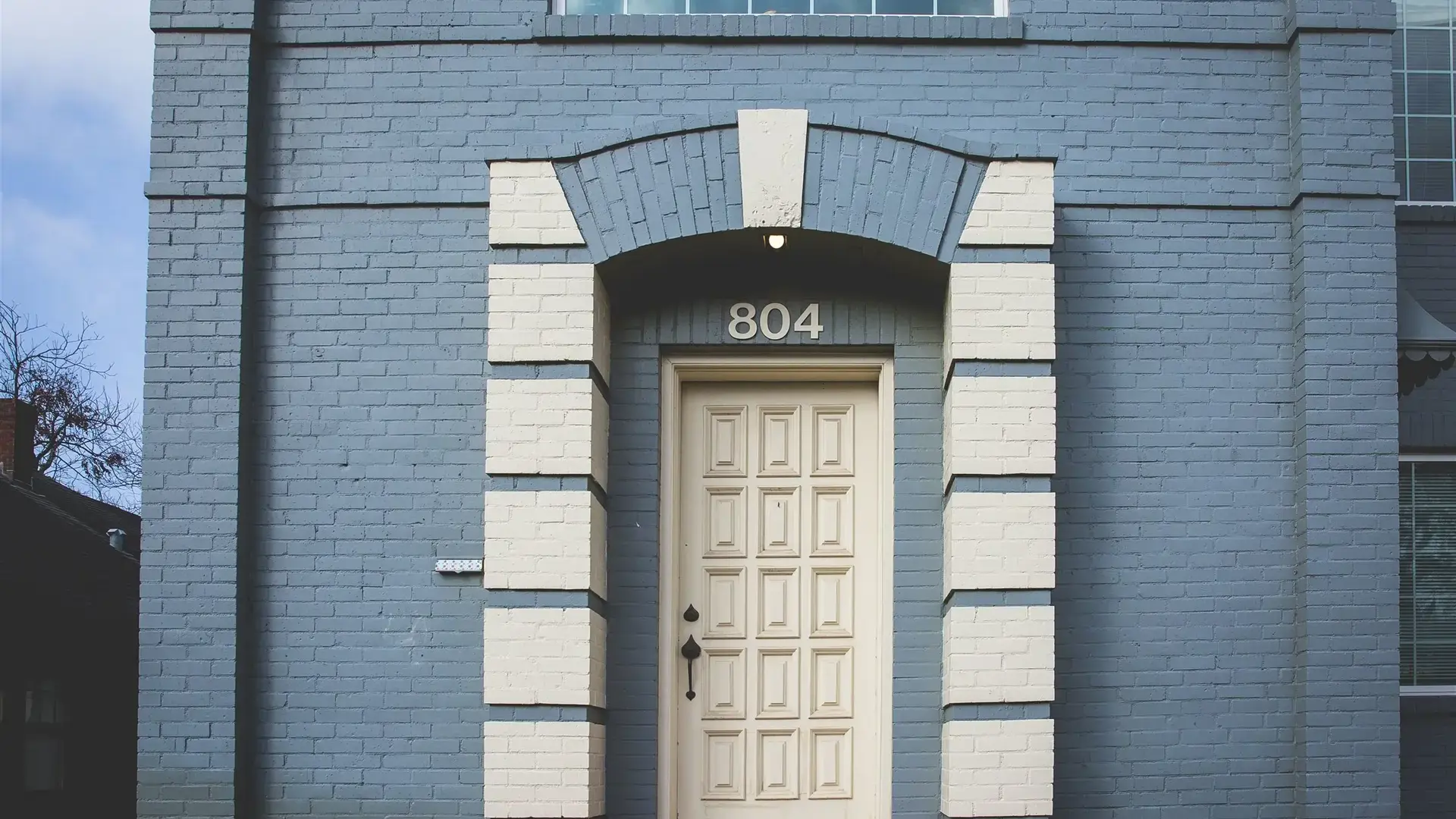 Front entrance of a blue brick building with a white arched doorway. Campus 804