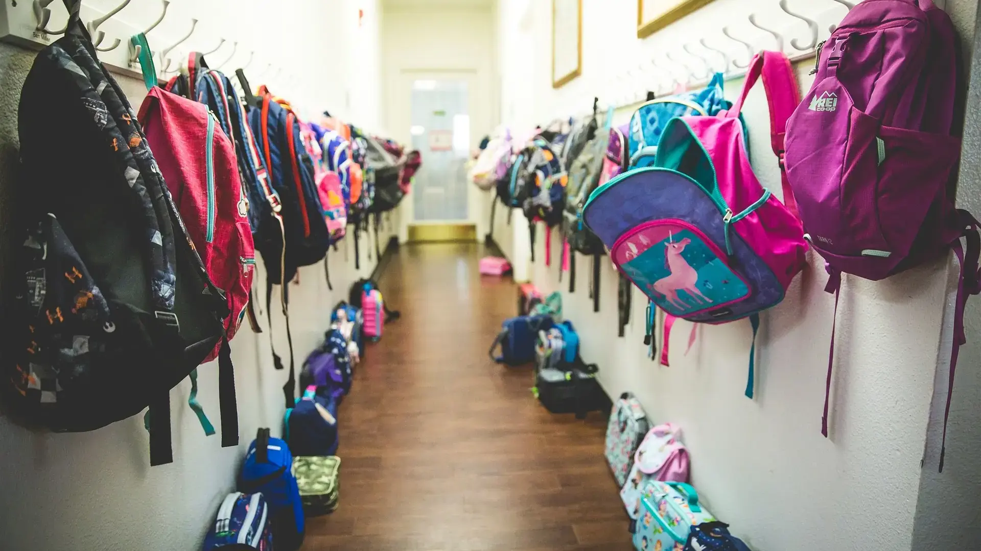 Rows of backpacks hanging on hooks in a school hallway.