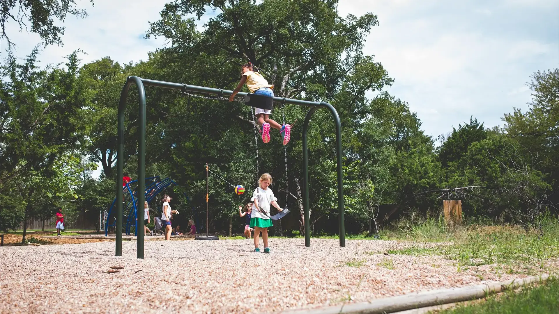 Children playing on outdoor playground equipment surrounded by trees.