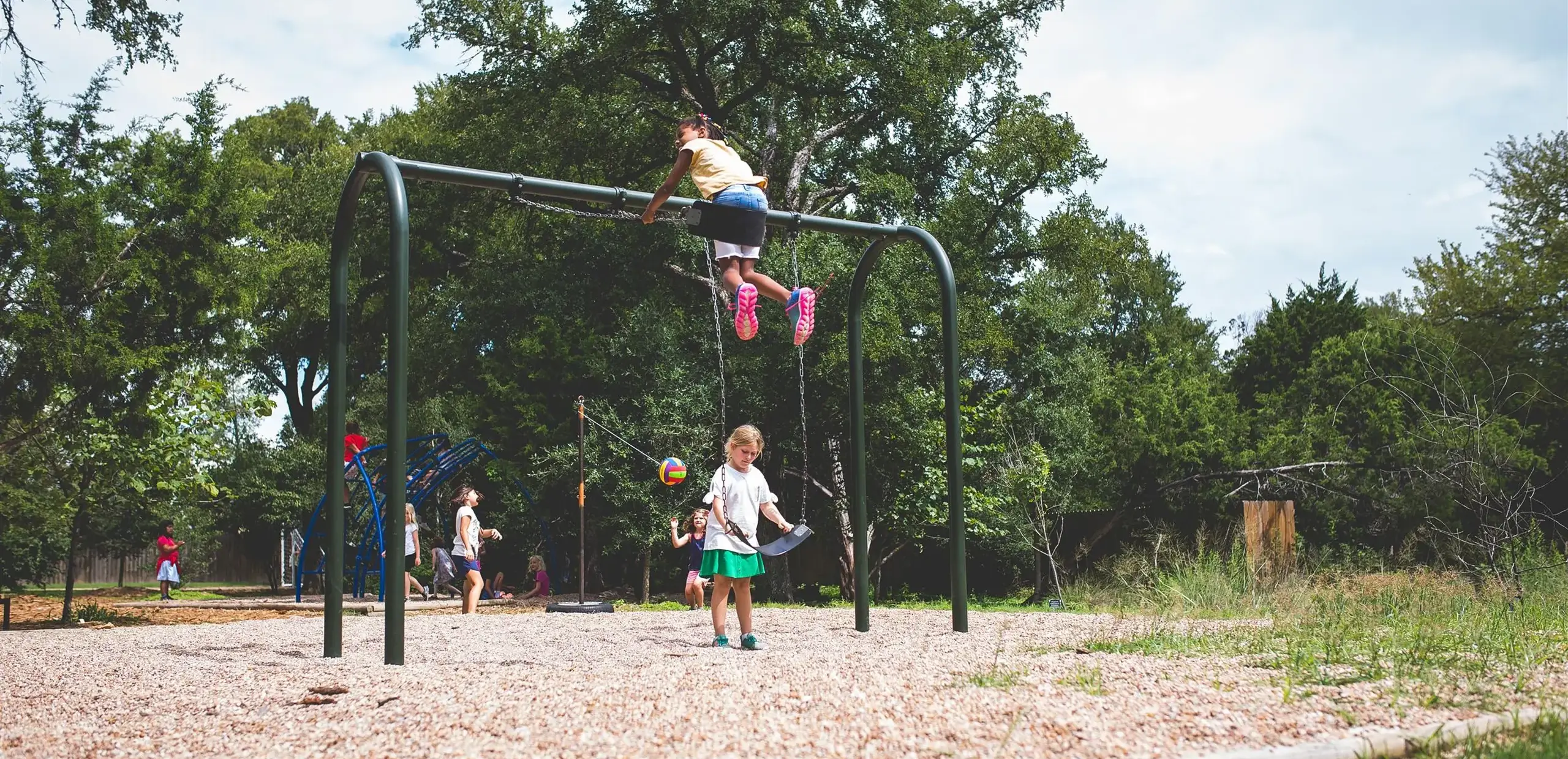 Elementary students playing on outdoor playground equipment, with one child sitting atop the swing set frame.