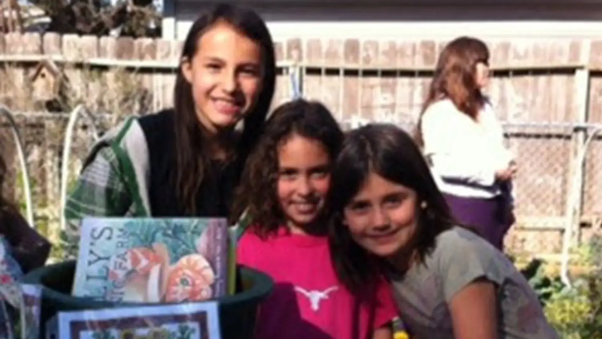Two students smiling together outdoors with a teacher standing behind them