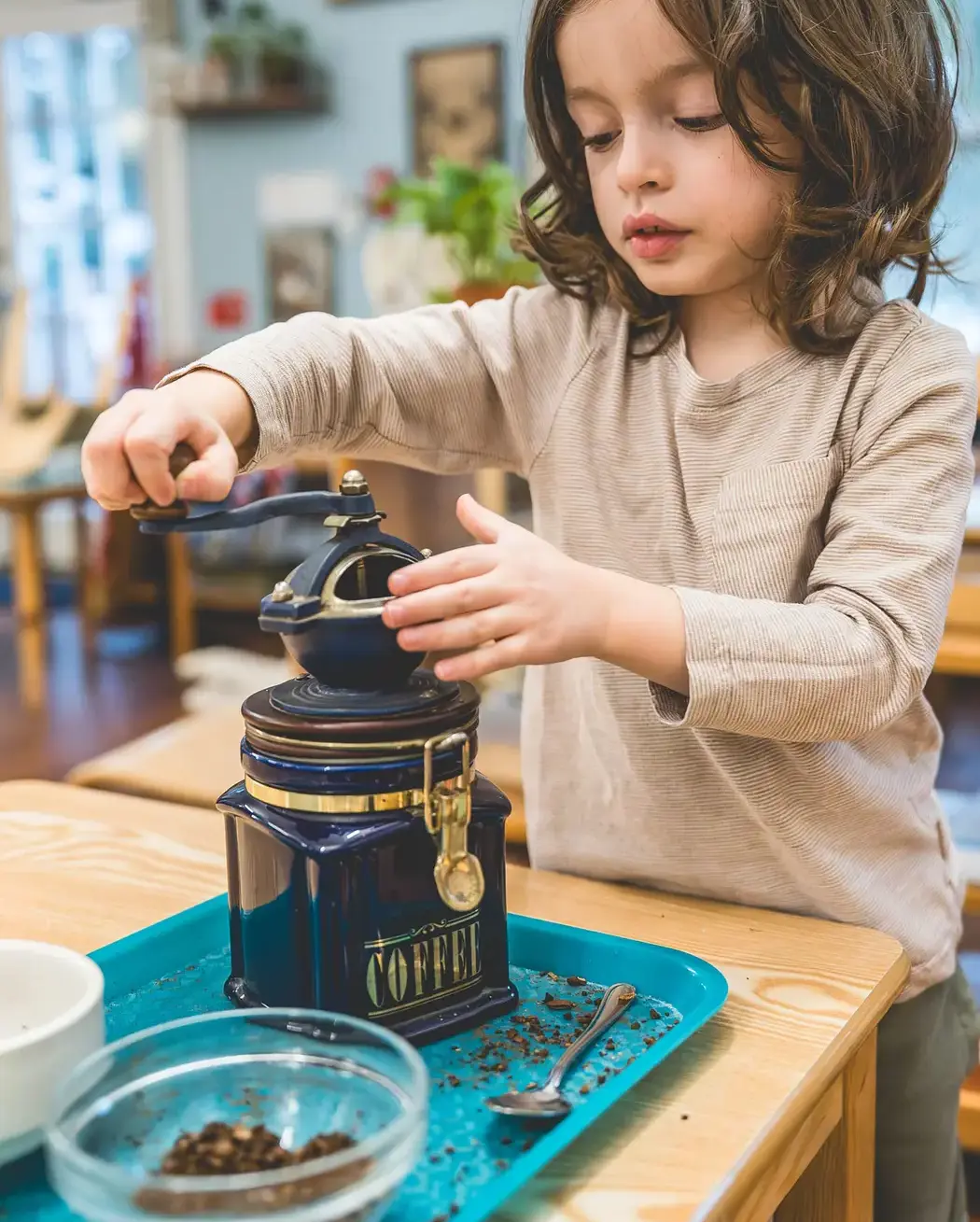 Young child using a hand-crank coffee grinder as part of a hands-on learning activity in an Early Childhood classroom.