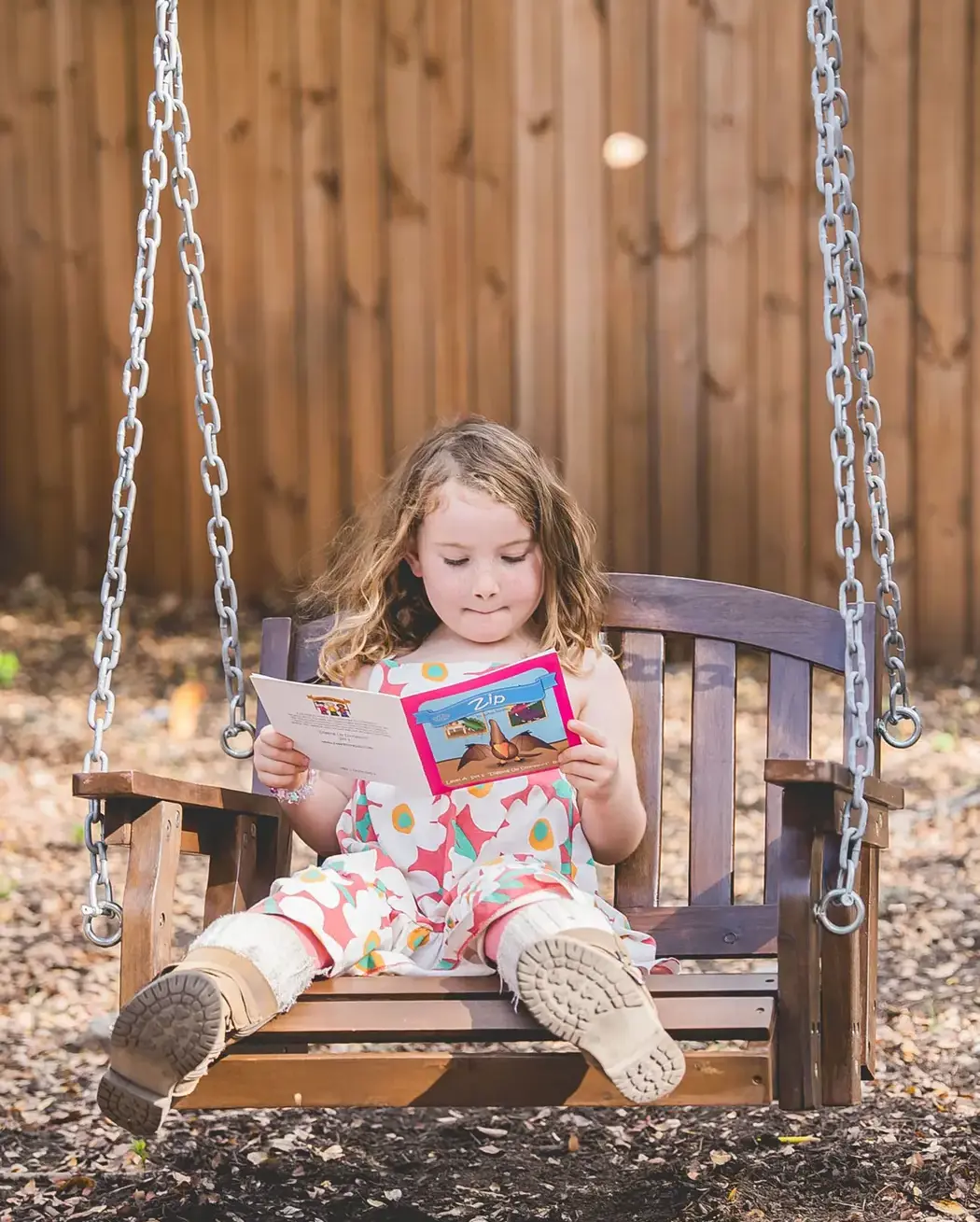 tudent enjoying independent reading on a wooden swing in an outdoor learning space.