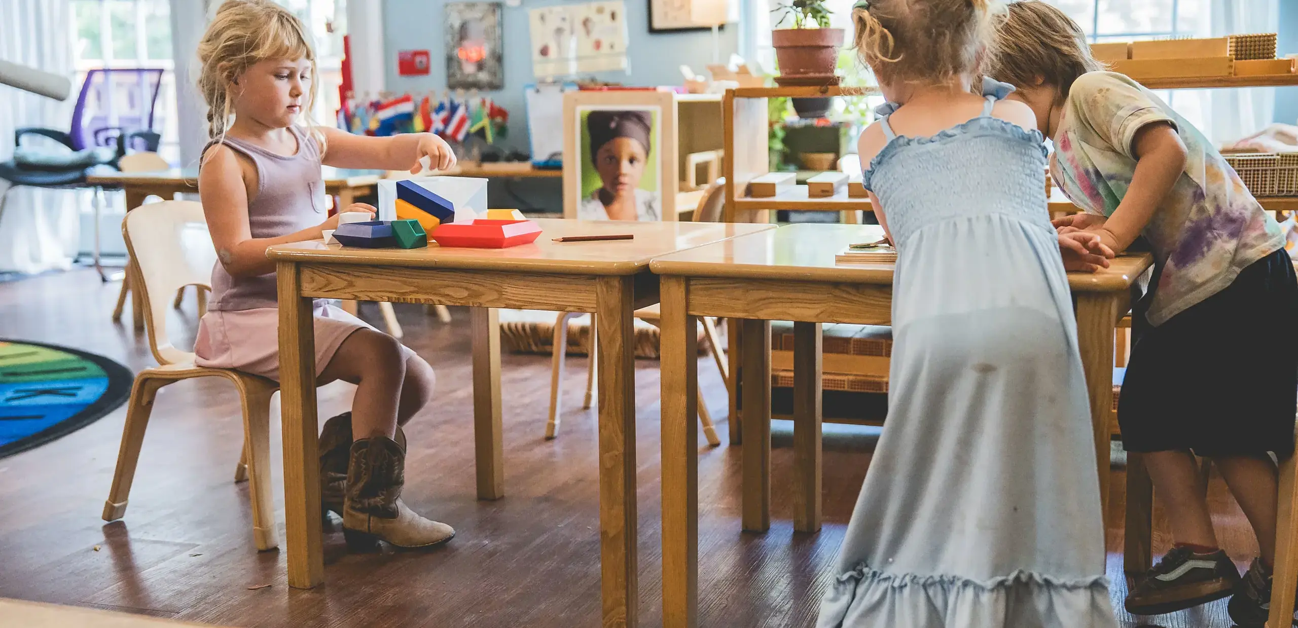 Young children working with colorful sensorial blocks at a table in a Montessori classroom.