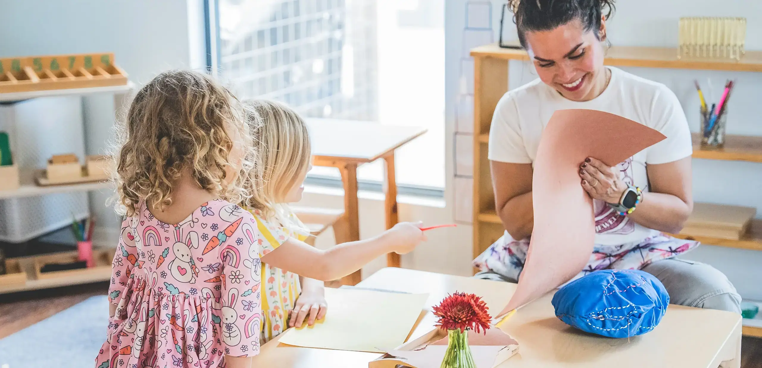 a teacher guiding young children through an art activity at a table.
