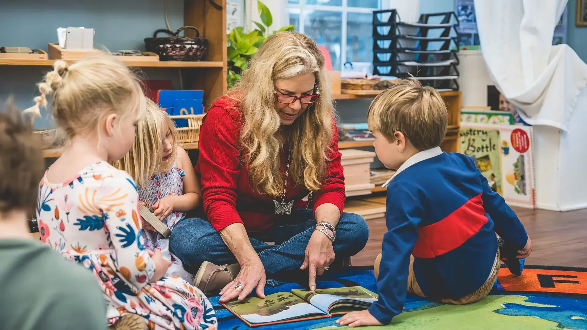 A teacher reading and engaging with young children seated on the floor.