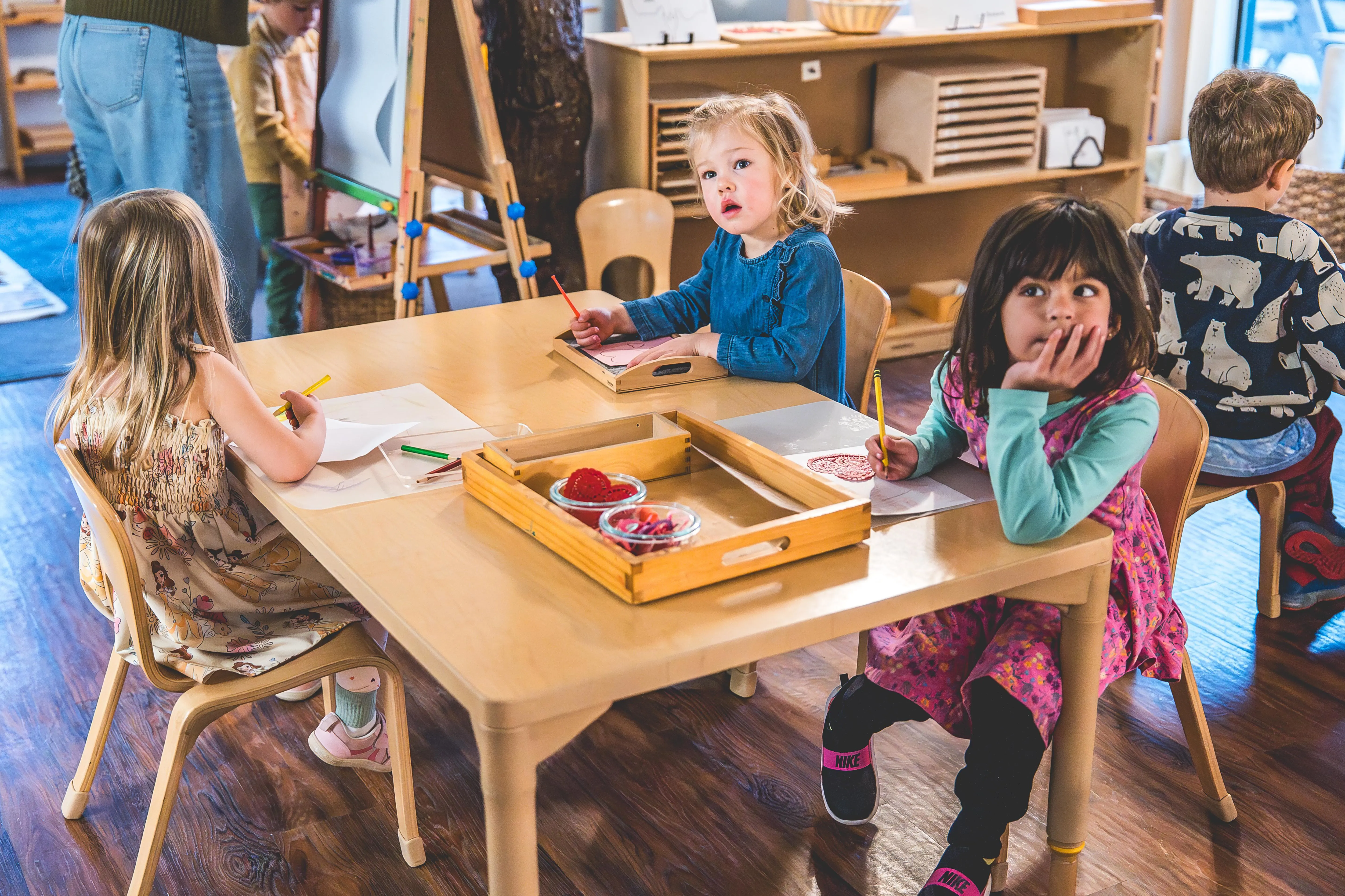 Primary students sit together at a classroom table drawing and working independently during Montessori work time.