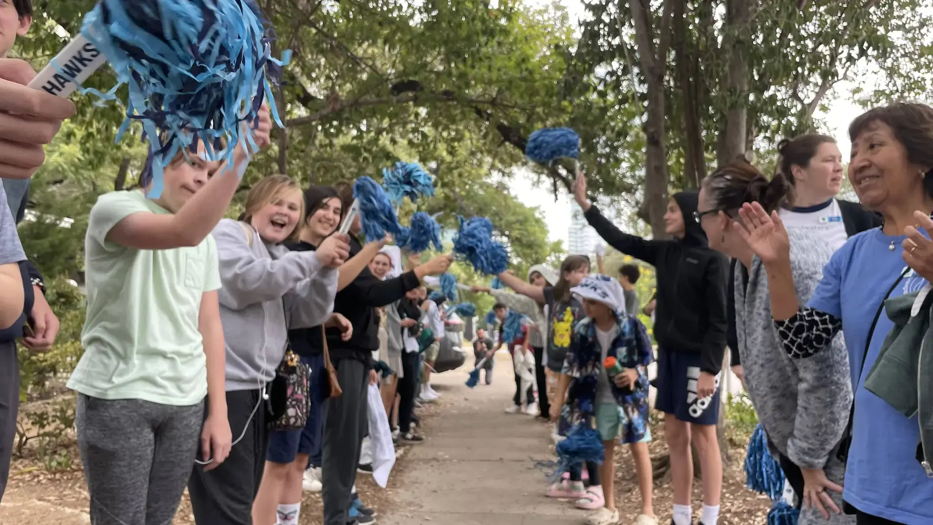 students waving blue and white pom-poms outdoors during a pep rally.