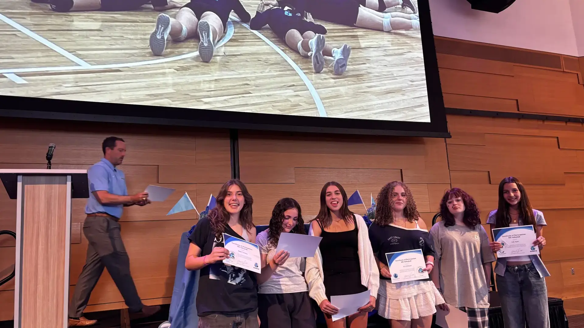 middle school students holding certificates on stage during an athletics awards ceremony.