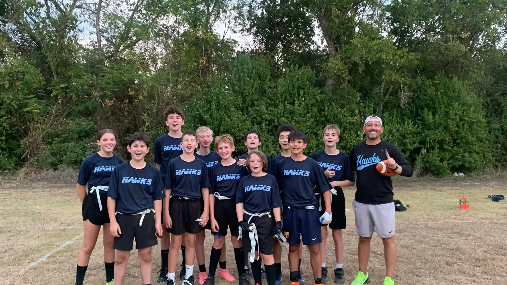 middle school flag football team posing together with their coach on the field.