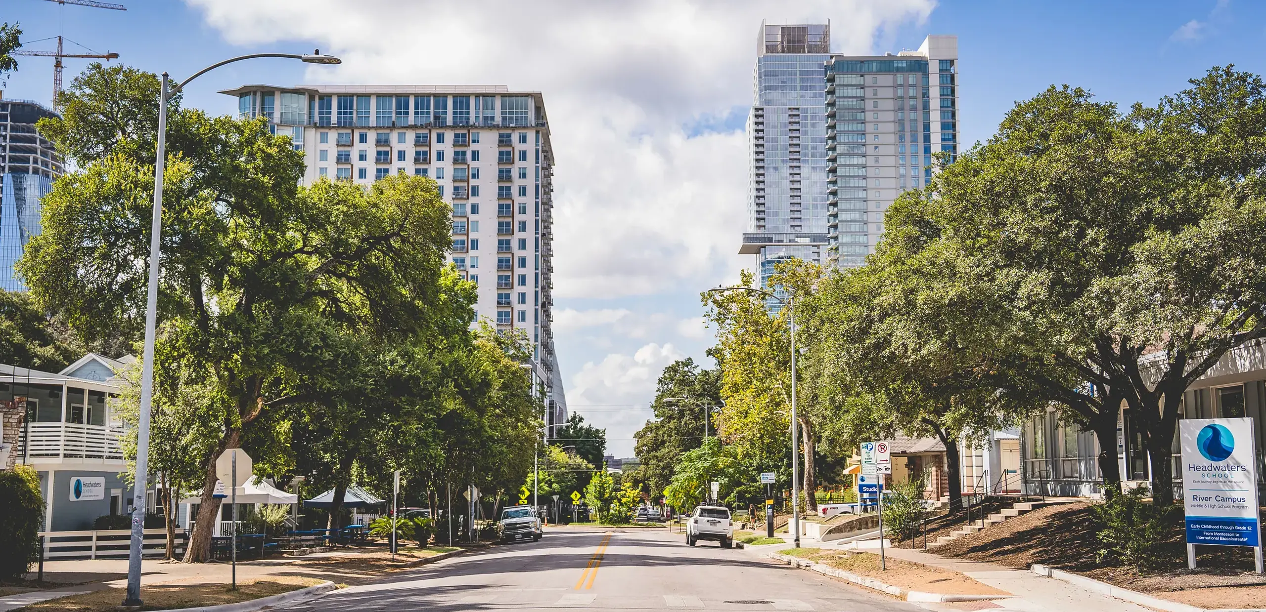 Street view of Headwaters School's River Campus for Middle and High School, with tree-lined buildings and downtown high-rises in the background.