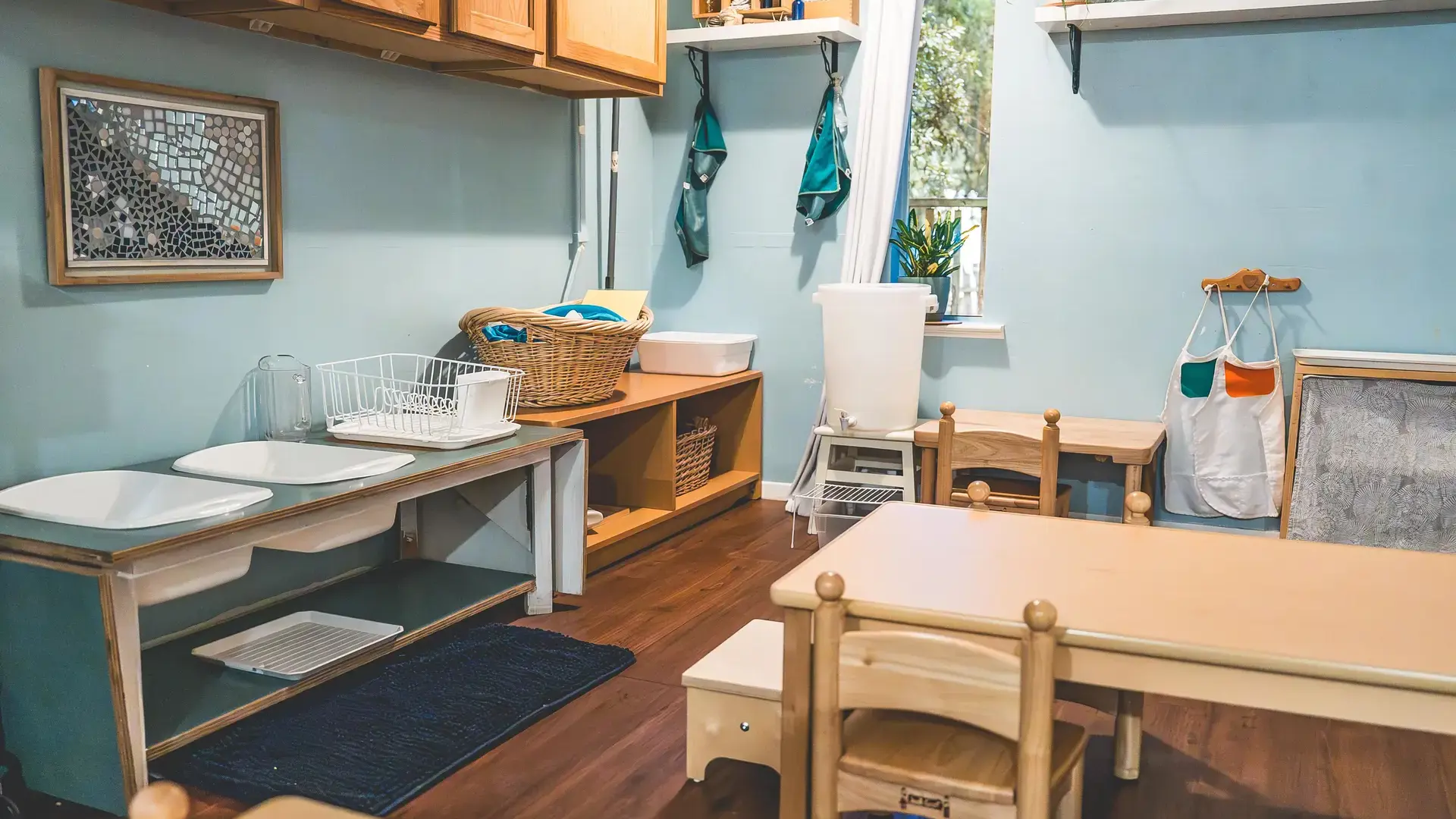 Montessori classroom with a practical life washing station and wooden tables.