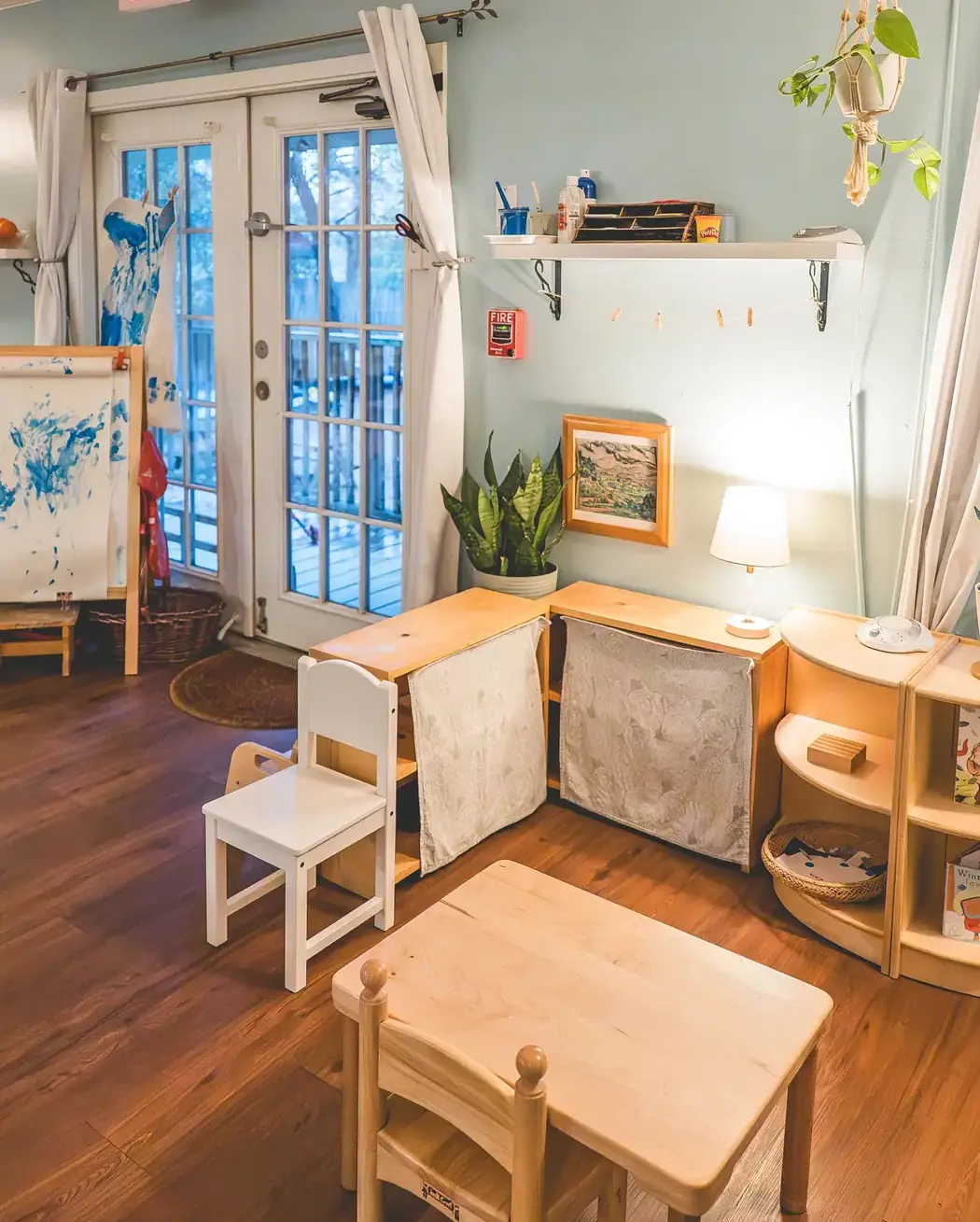 Empty Montessori classroom with wooden child-sized furniture, shelving, and a cozy reading corner.