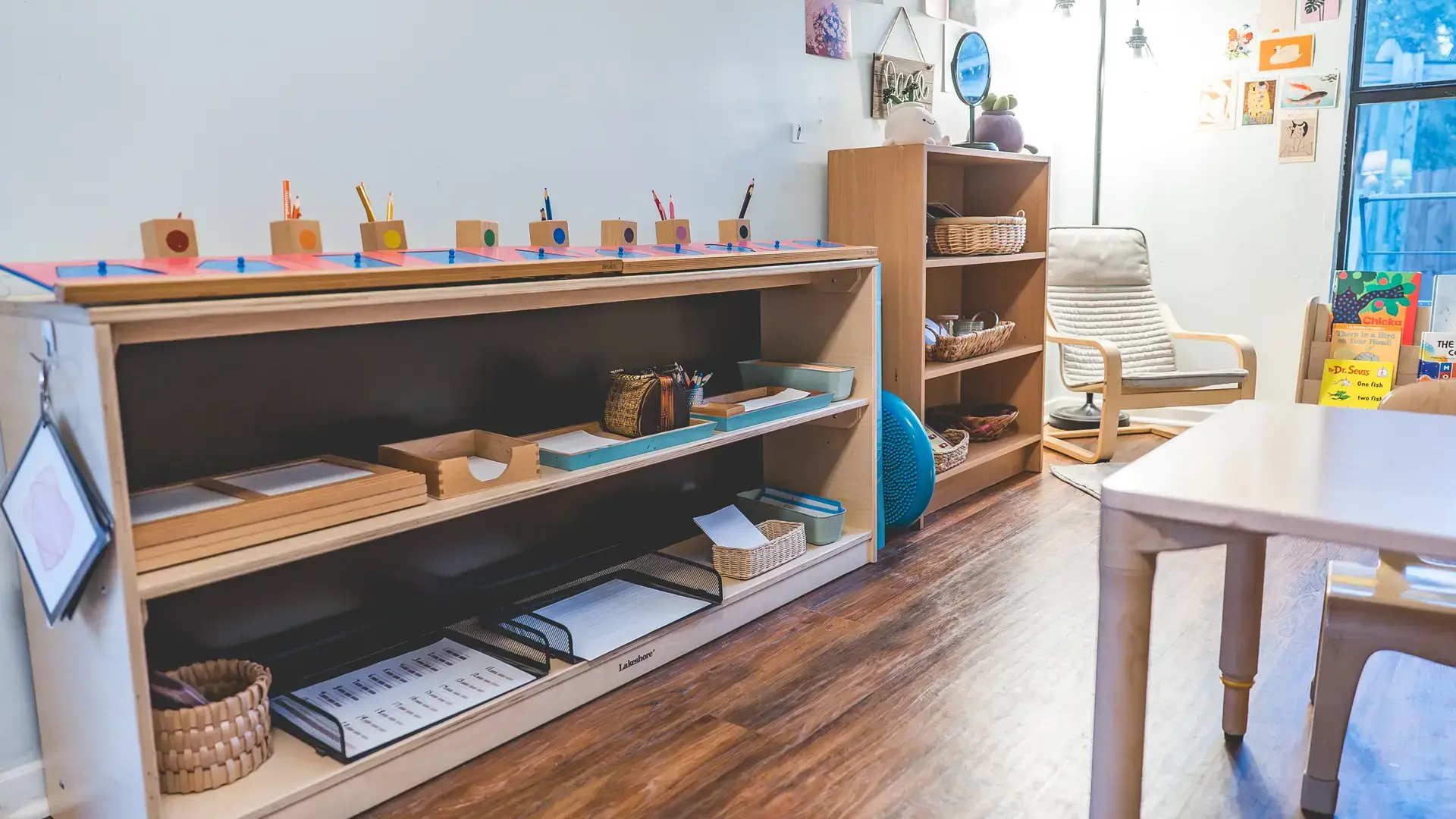 primary classroom shelf with Montessori materials and low tables.