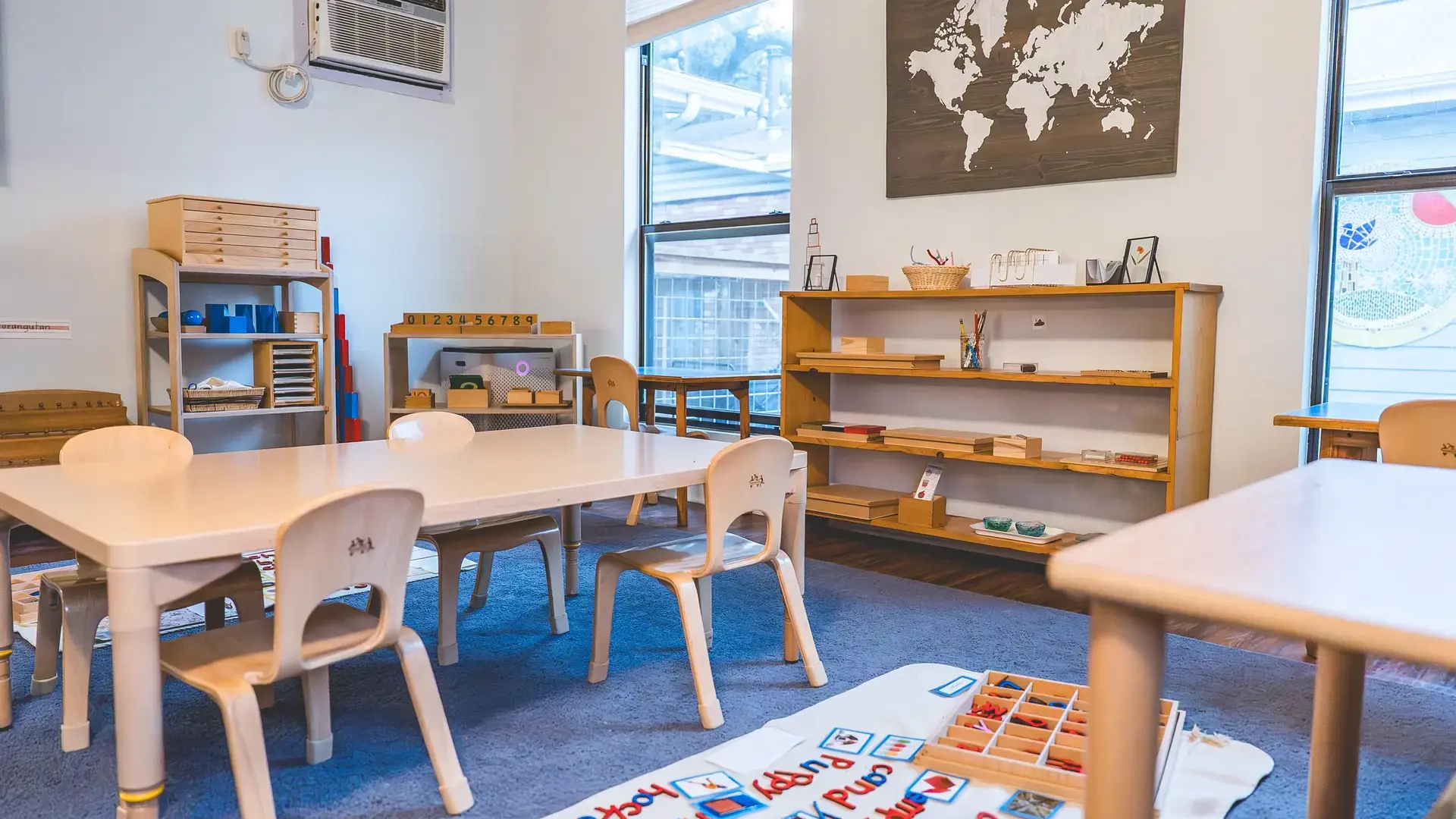 primary classroom with low wooden tables, chairs, and a world map.