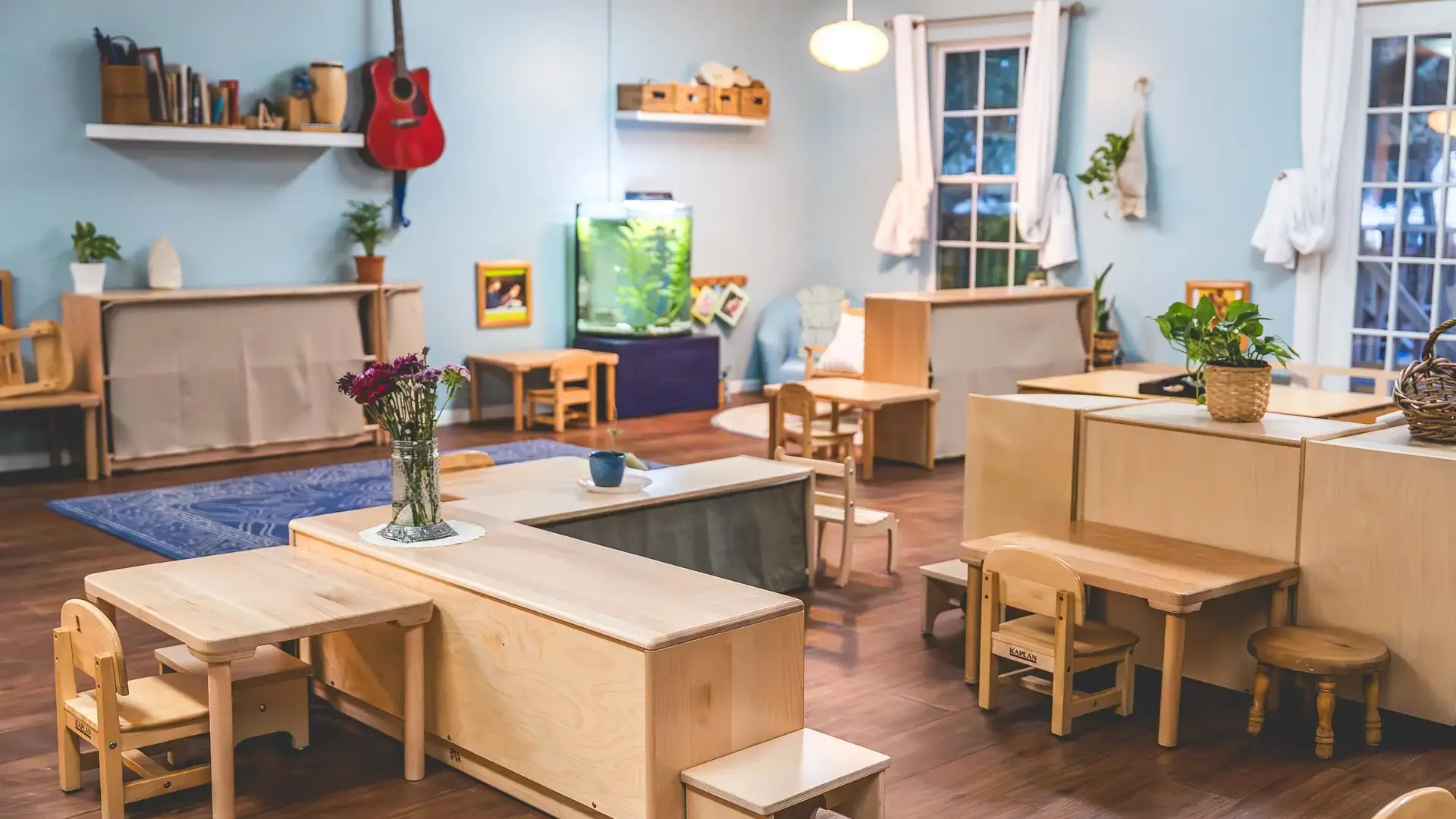 Montessori classroom with wooden tables, chairs, and shelving.