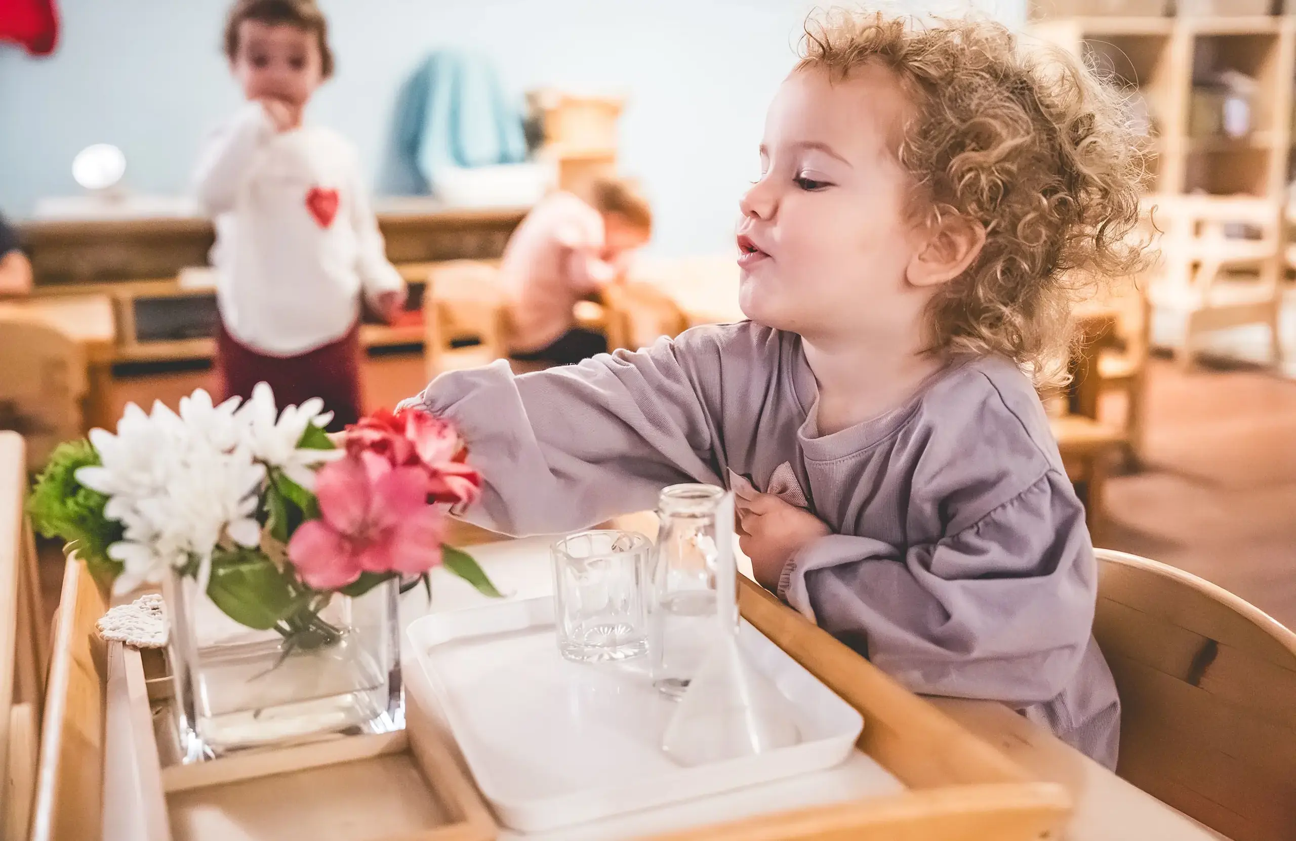 Young child carefully arranges flowers in a vase during a practical life activity in an early childhood Montessori classroom at Headwaters School.