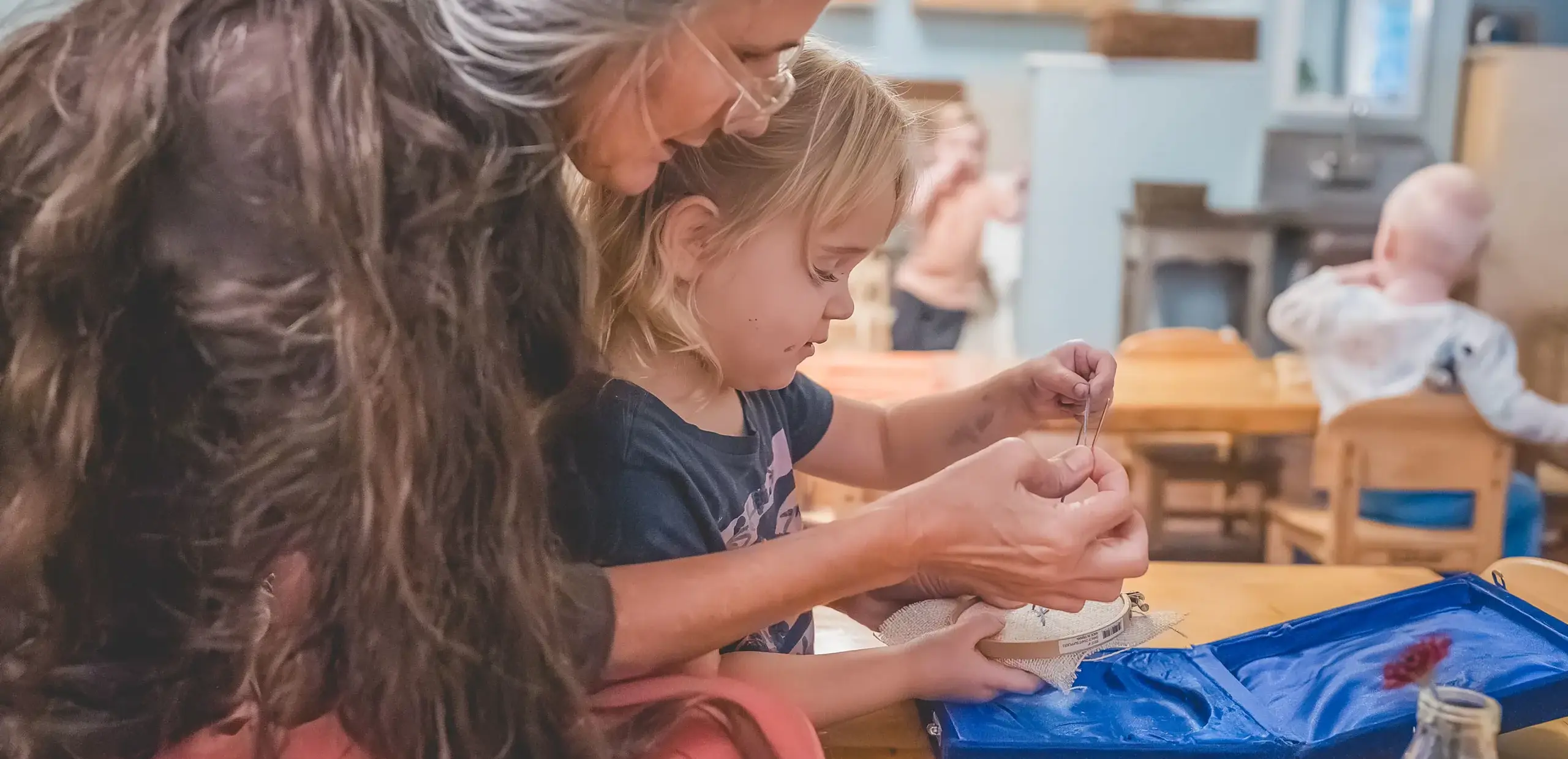 A teacher guiding a young child through a Montessori practical life sewing activity