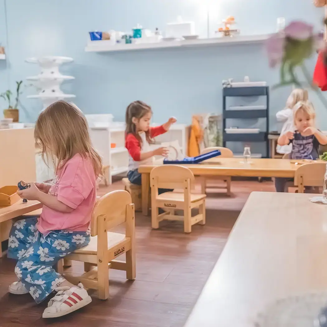 young students working independently at low tables in a Montessori classroom.
