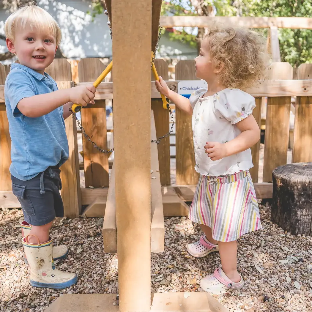 Two Young Children’s Community students play together outdoors on a playground structure during recess.